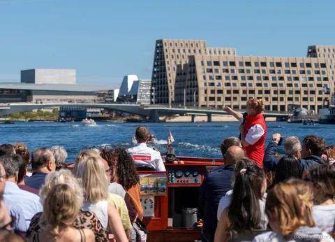 Guide berättar om kanalrundturen i Köpenhamn nära statyn av Den Lilla Sjöjungfrun